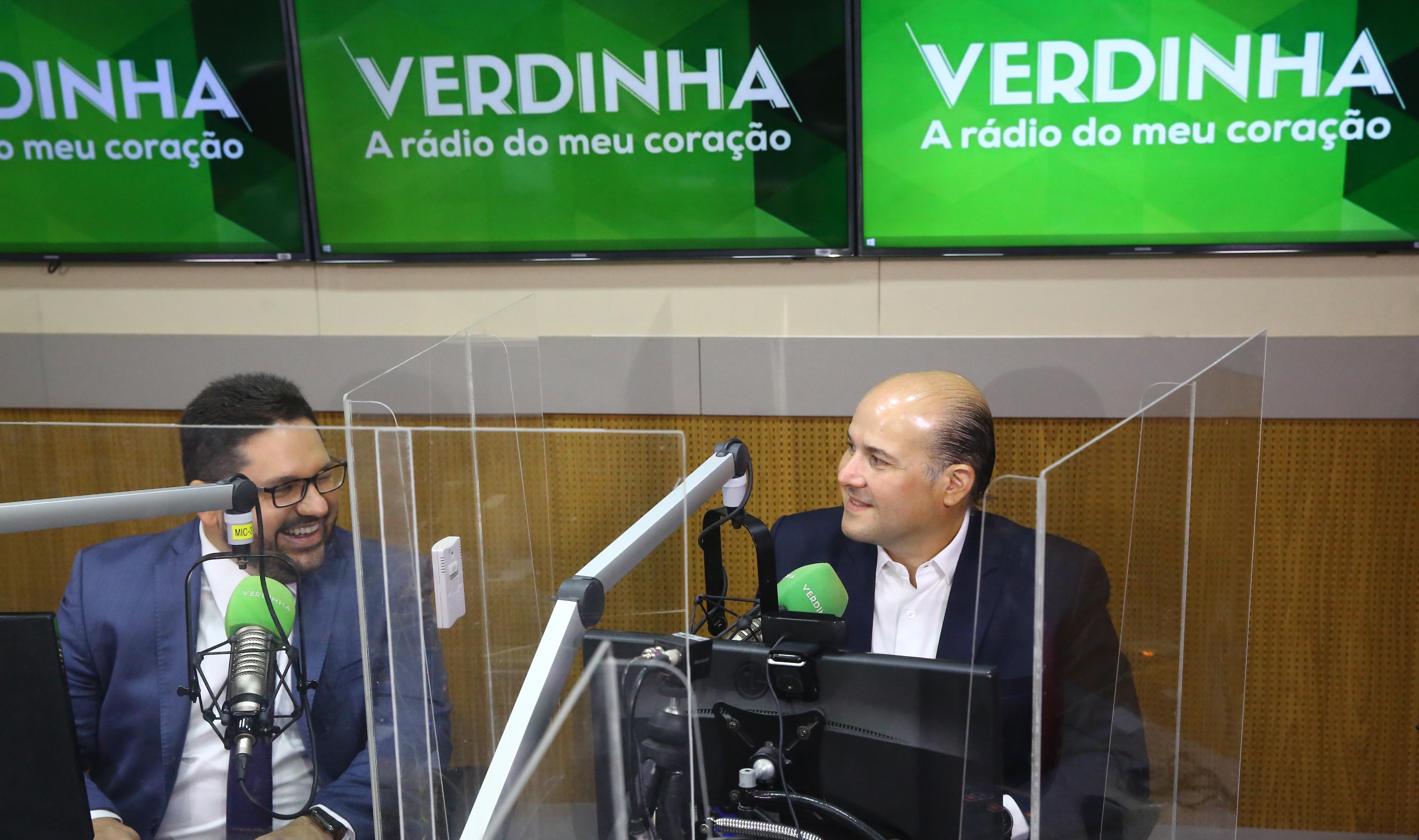 Inácio Aguiar e prefeito lado a lado se olhando e sorrindo em estúdio de rádio